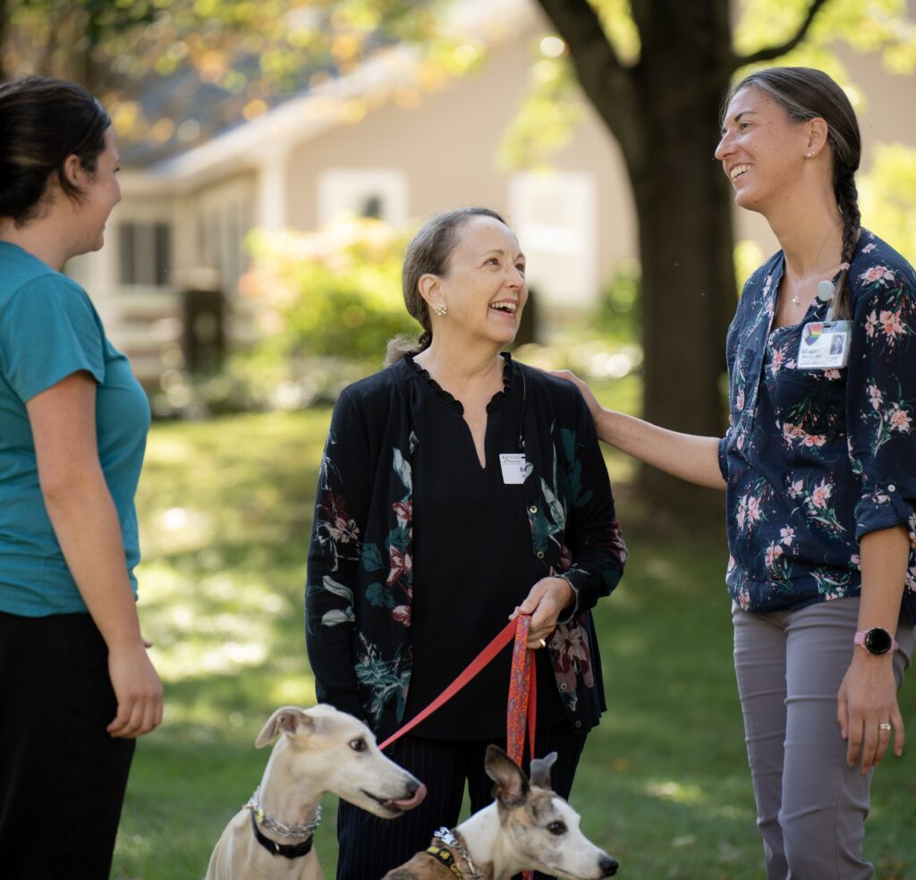 Three women talking outdoors with two dogs.